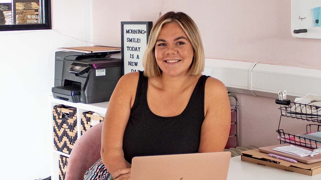 Jess Treatboxes corporate superstar sitting in TreatBox HQ behind a desk and pink laptop.