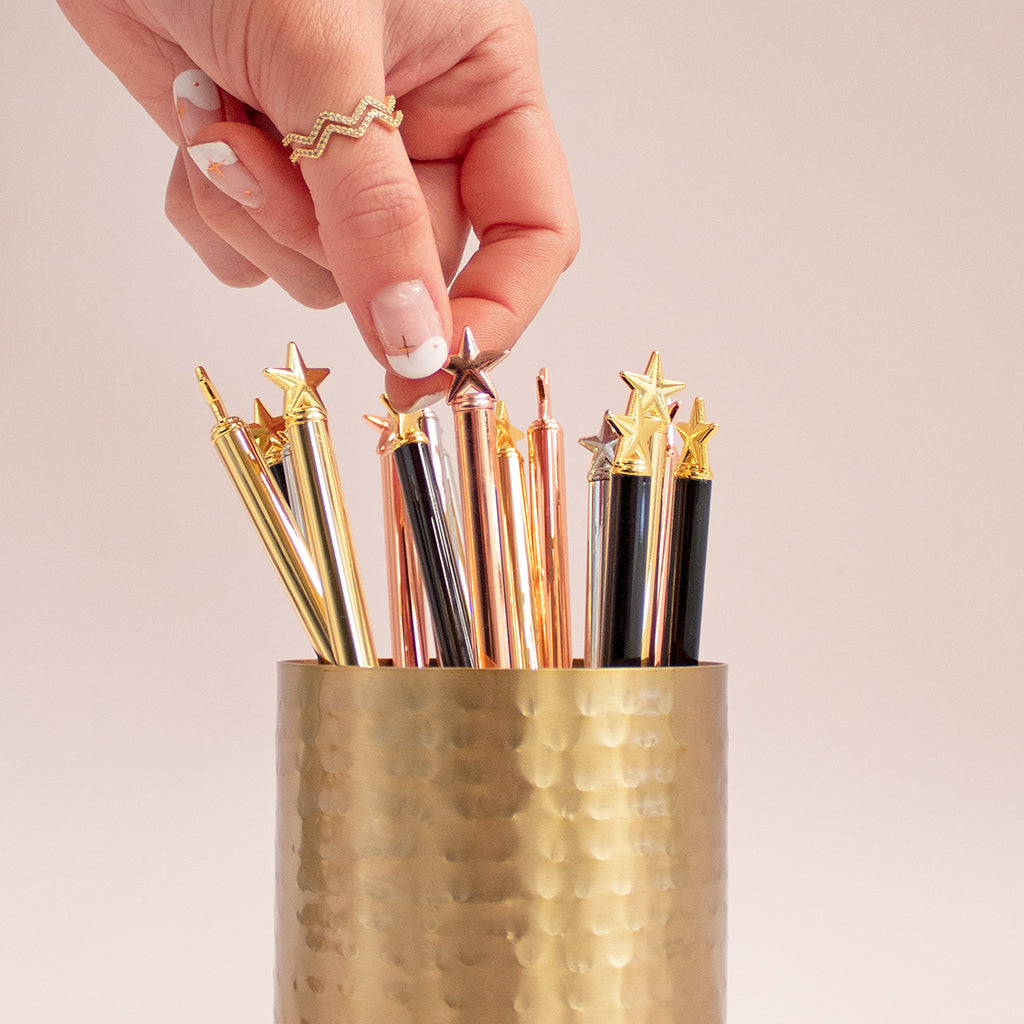 gold pens in a gold jar with star topper