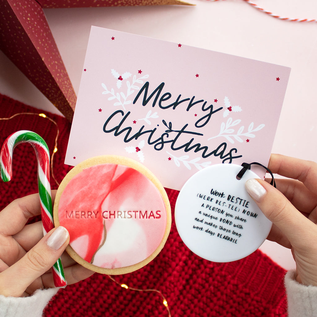Hands holding a Merry Christmas postcard, candy cane, biscuit and keepsake ceramic with a red jumper bakground