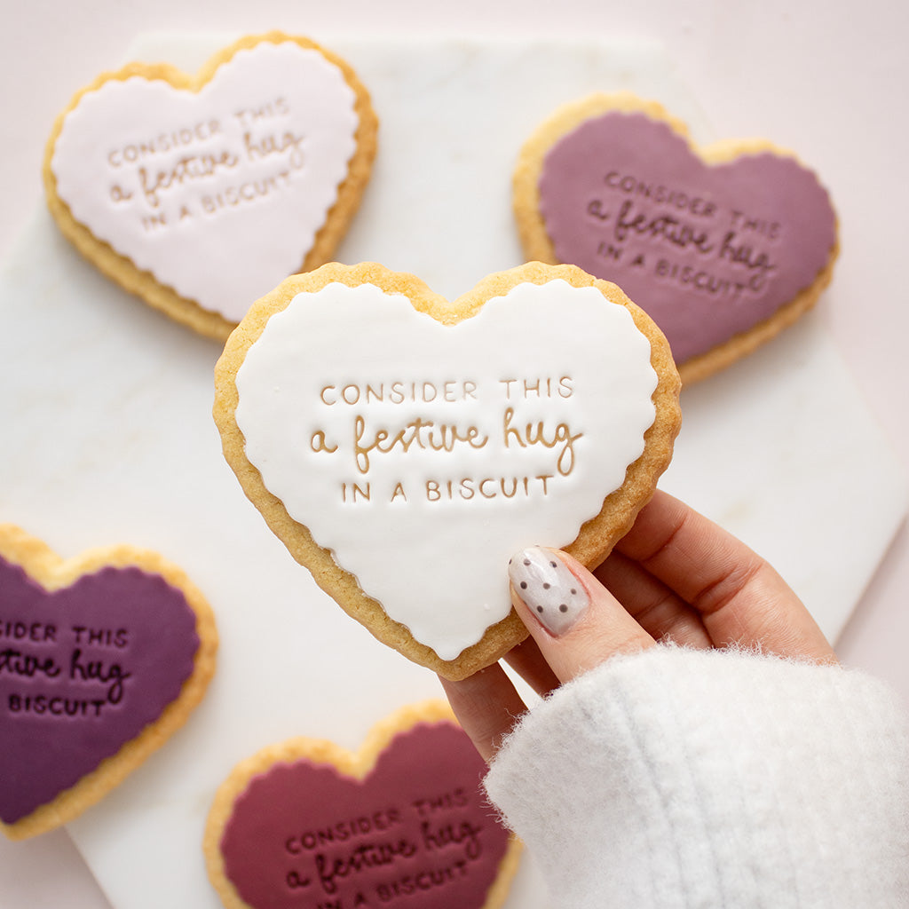 Heart-shaped shortbread cookiess decorated with icing and the phrase 'CONSIDER THIS a festive hug IN A BISCUIT',