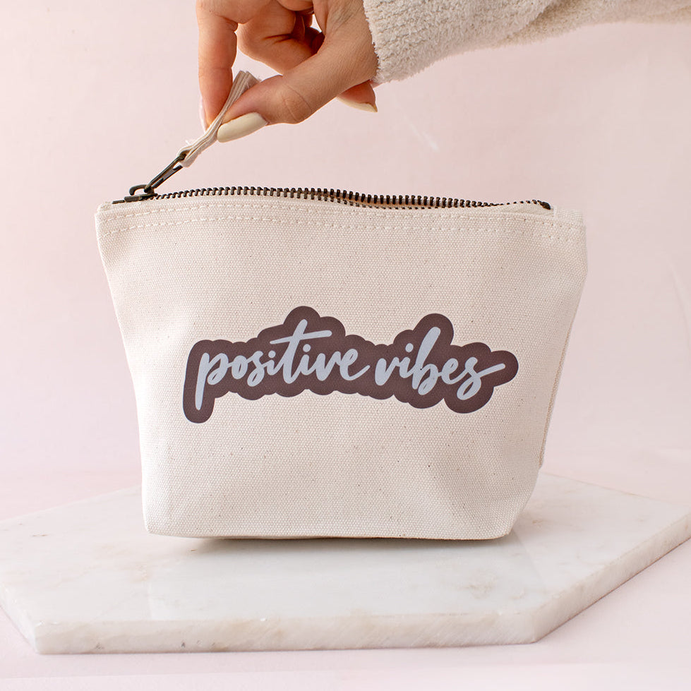 white canvas pouch with positive vibes slogan in blue and brown fun font style writing