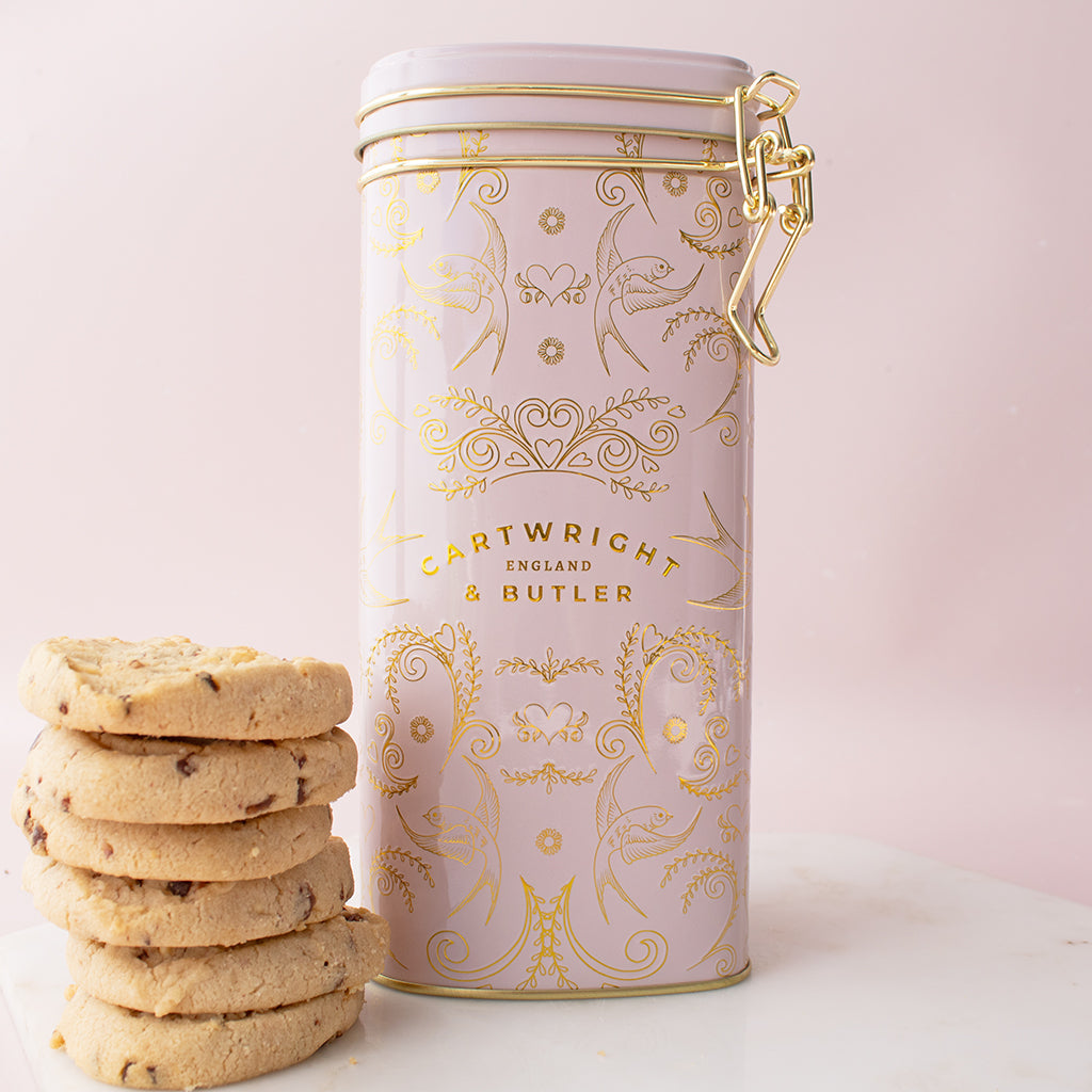 Decorative cookie tin with gold patterns and a stack of cookies on a light pink background