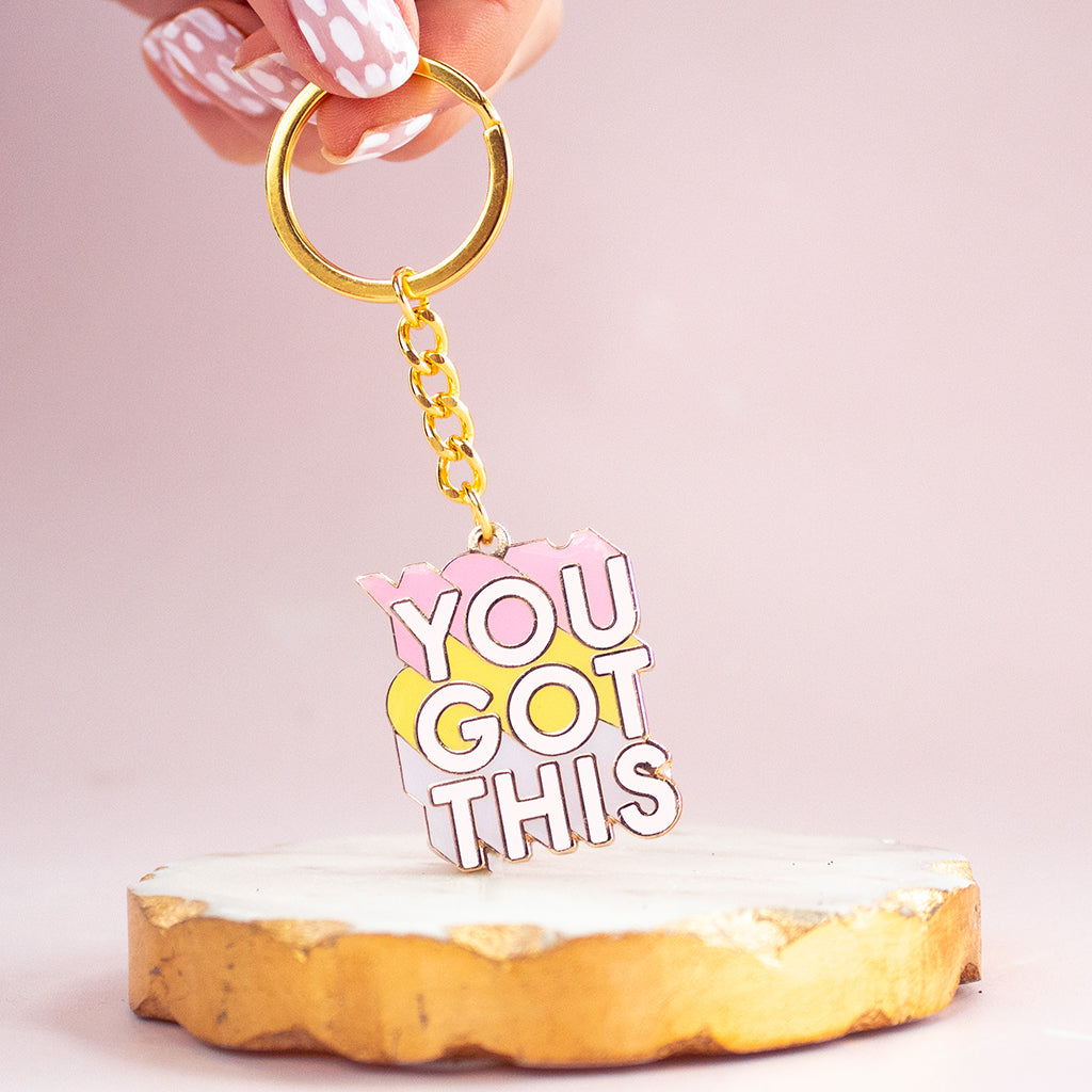 Fingers holiding a gold keyring with the words You Got This