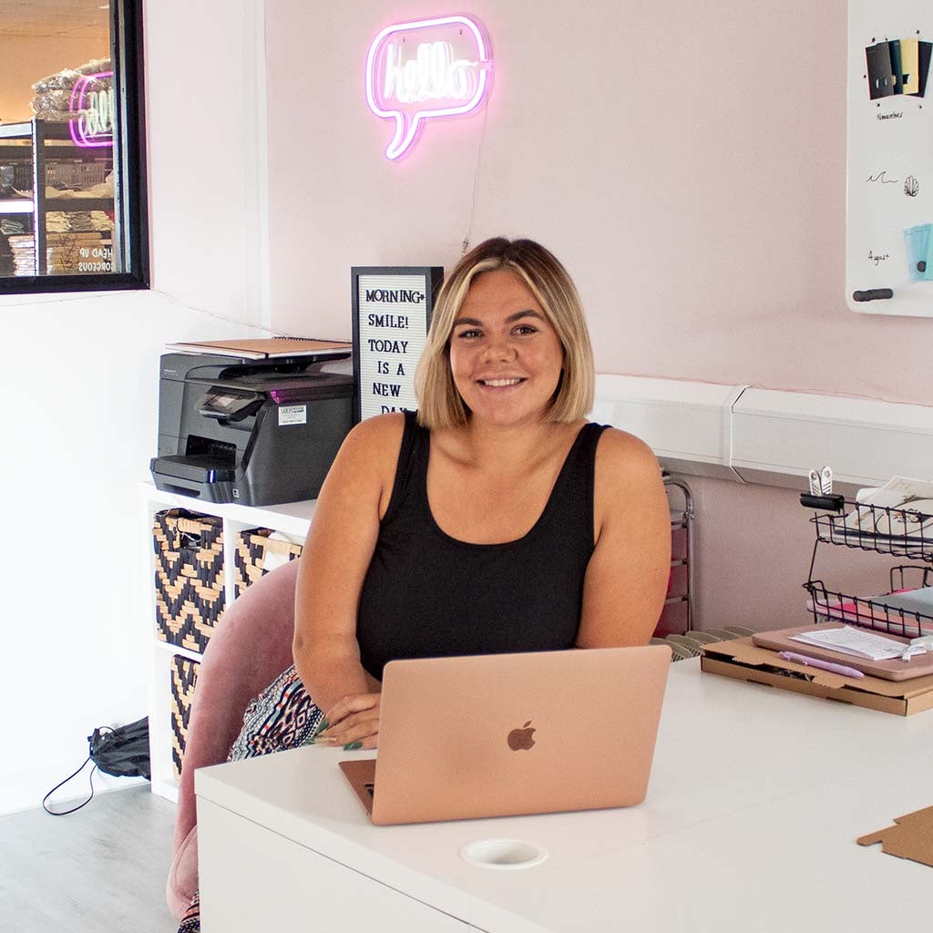 Jess Treatboxes corporate superstar sitting in TreatBox HQ behind a desk and pink laptop.