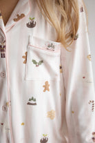 Close-up of a person wearing light pink ribbed pajama top with a holiday print, featuring gingerbread men, holly, stars, and a chest pocket with a matching patch.