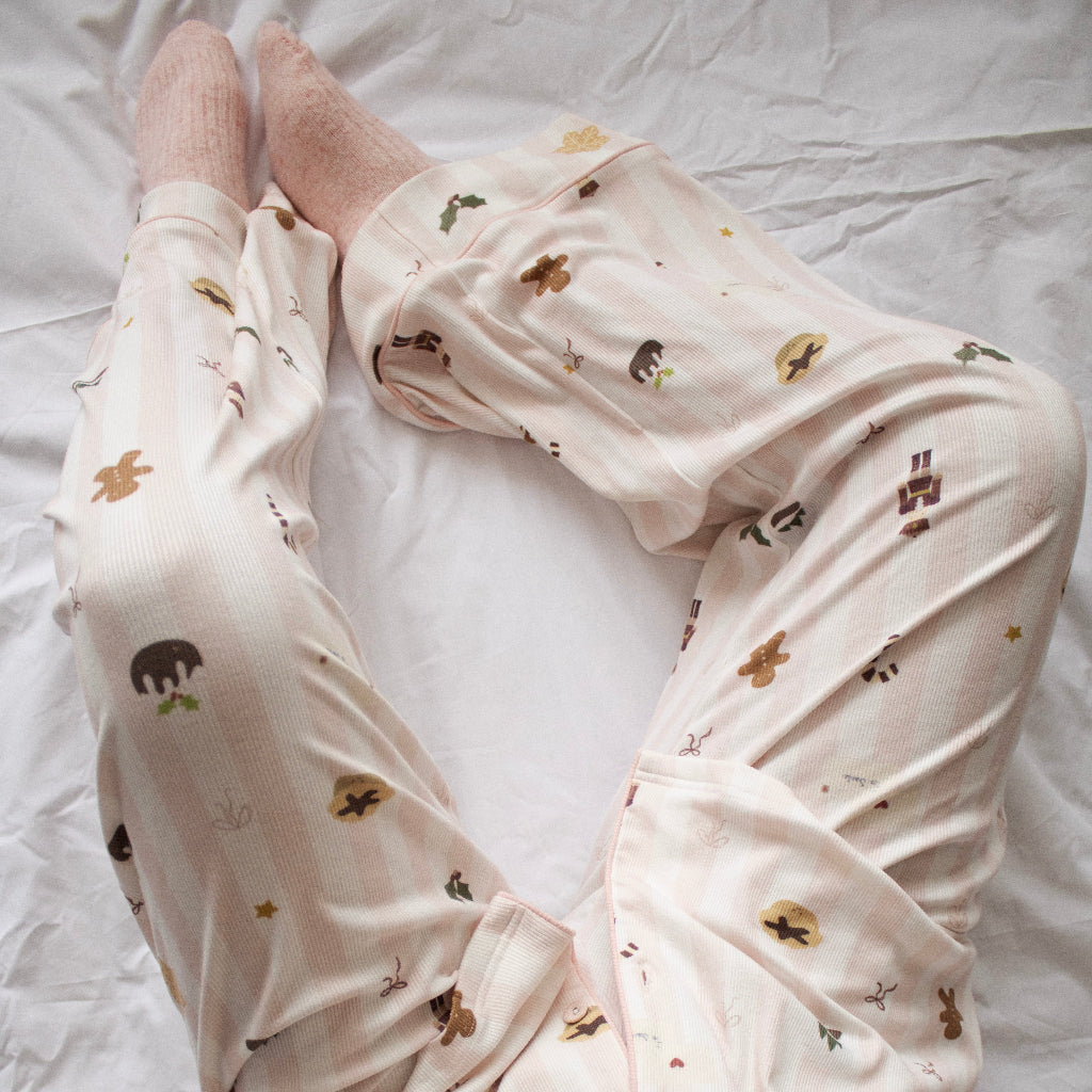 A person wearing light pink pajama pants with a small animal print and matching socks, lying on a white bed.