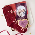 A holiday gift set featuring a pair of deep red crew socks with white bow and star patterns, a custom photo card, a heart-shaped sugar cookie, and a red envelope, arranged in a box with white tissue paper.