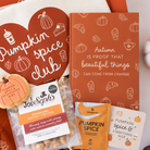 A styled autumn gift set featuring a white bag with a large red heart that reads 'Pumpkin spice club,' an orange book with white line drawings, a cookie labeled 'Pumpkin Spice & Everything Nice,' a bag of Joe's Pops pumpkin spice gourmet popcorn, a Blendworks pumpkin spice snack pouch, and a card reading 'Pumpkin Spice & Everything Nice.'.