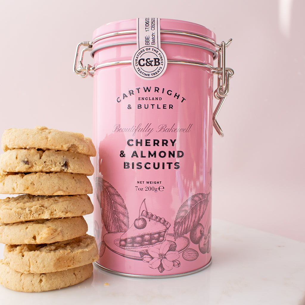 Pink canister of Cartwright & Butler cherry and almond biscuits with cookies on a light pink background