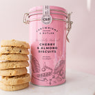Pink canister of Cartwright & Butler cherry and almond biscuits with cookies on a light pink background