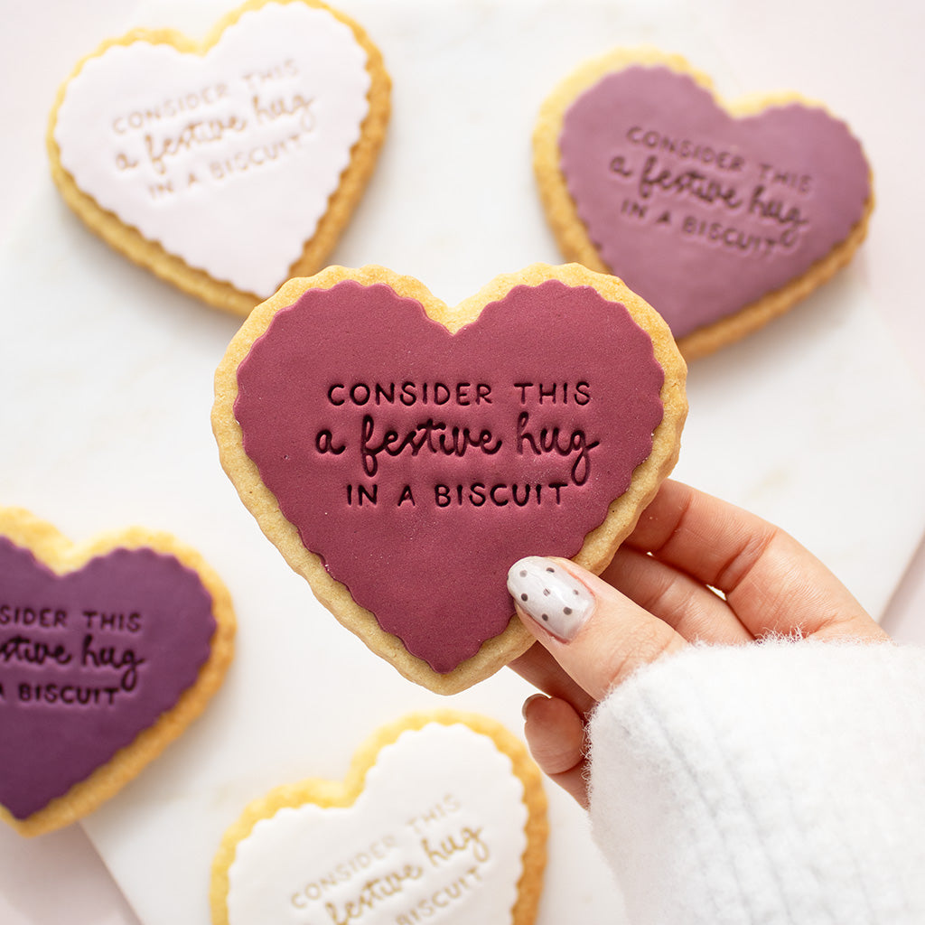 Heart-shaped shortbread cookiess decorated with icing and the phrase 'CONSIDER THIS a festive hug IN A BISCUIT', 