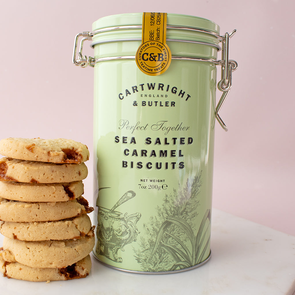 Green tin of Cartwright & Butler sea salted caramel biscuits with cookies on a light pink background